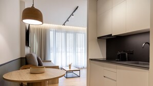 A modern kitchen with a dining area, featuring a round wooden table, chairs, a coffee machine, and a pendant light. - Rebalance Apartments (Athens)