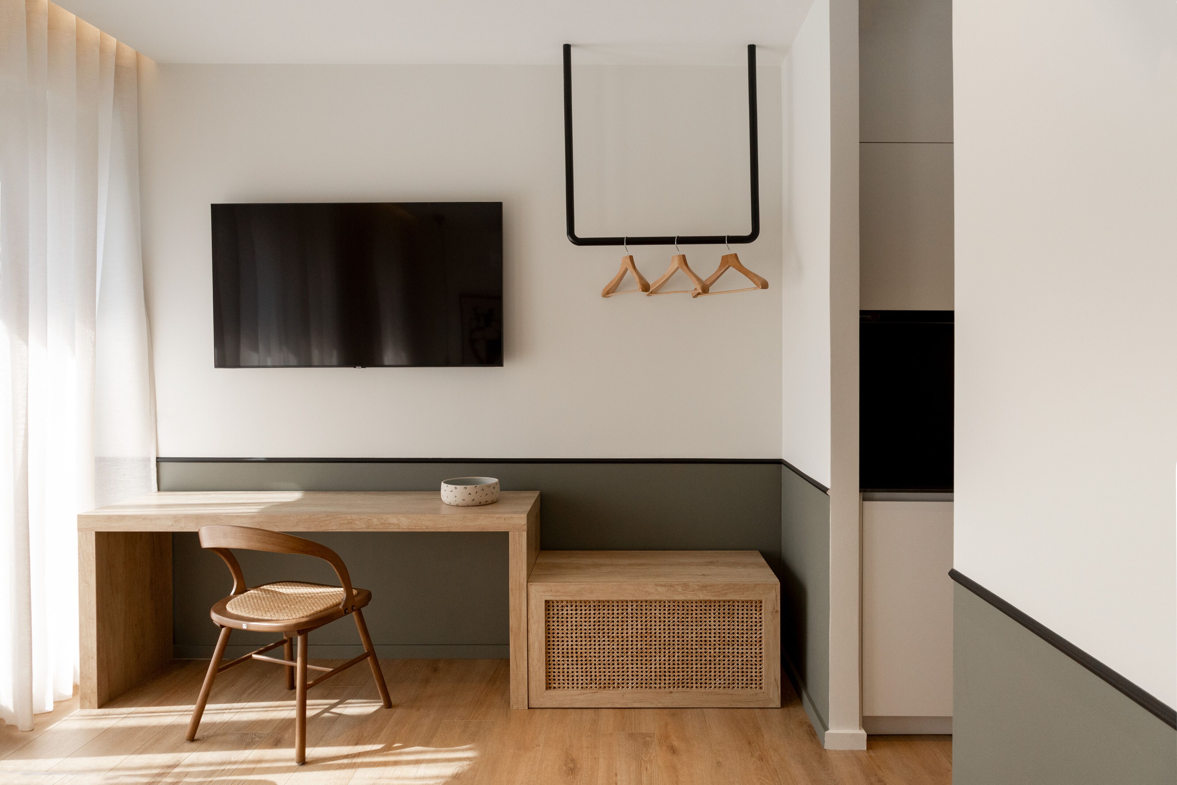 Een moderne kamer met een houten bureau, een stoel, een televisie en een kapstok.