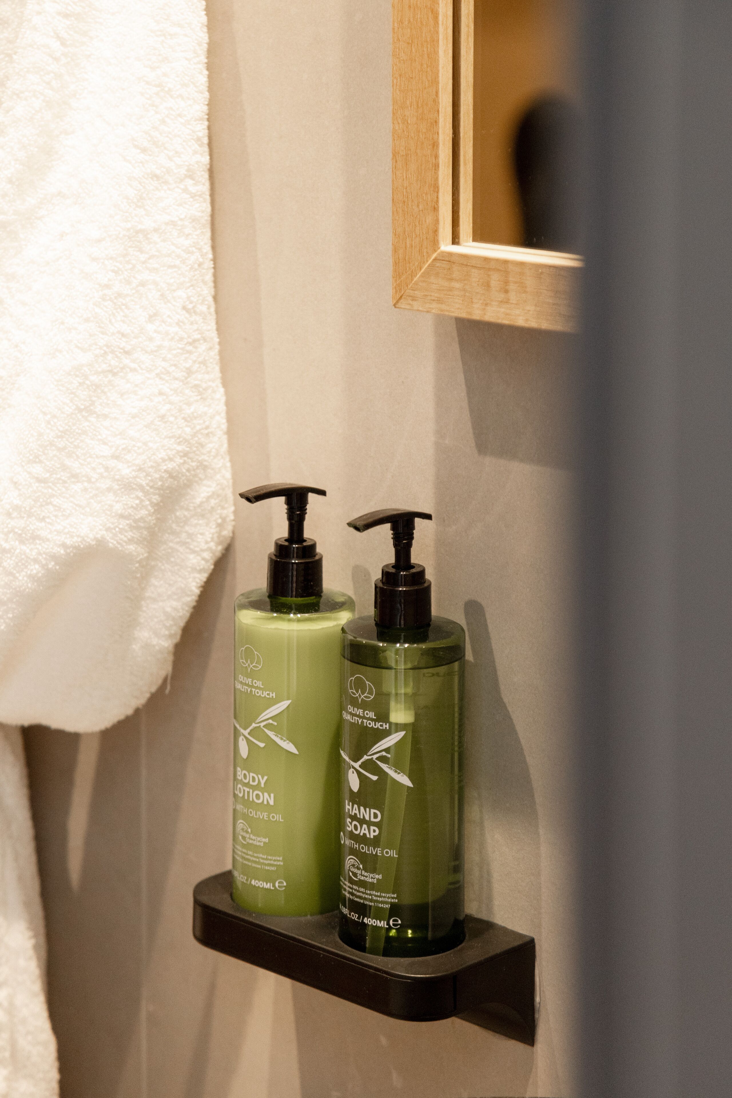 A bathroom with a shelf holding two bottles of olive oil body lotion and hand soap.