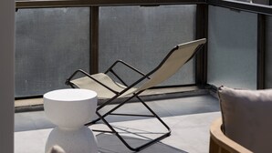 A balcony with a view of a cityscape and mountains. There is a chair, a small round table, and a wooden chair. - Rebalance Apartments (Athens)