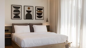 A modern bedroom with a wooden platform bed, white bedding, and abstract wall art. - Rebalance Apartments (Athens)