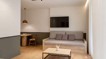 Ett modernt vardagsrum med ett soffbord i trä, en grå soffa, ett runt matbord och en hängande taklampa.