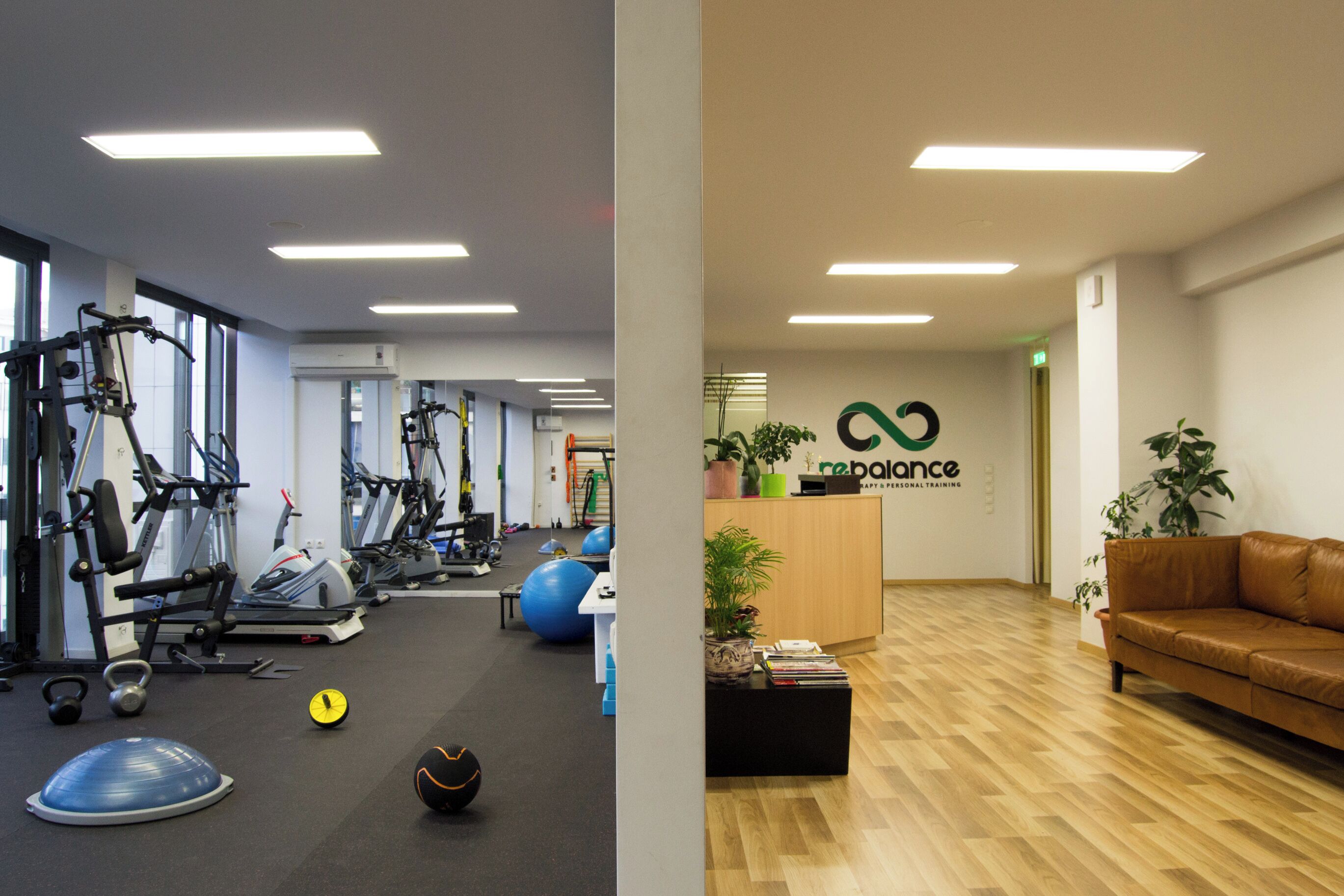 Ein Fitnessraum mit Trainingsgeräten und einer Rezeption mit einer Couch und Pflanzen.