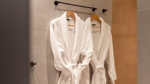 A bathroom with two white robes hanging on a rack, a wooden cabinet, and a tiled floor. - Rebalance Apartments (Athens)