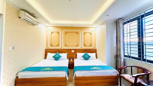 A hotel room with two beds, a wooden headboard, a window with blinds, and a chair.