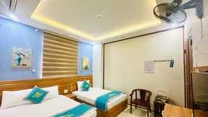 A hotel room with two beds, a desk, a chair, a fan, and a sliding door.