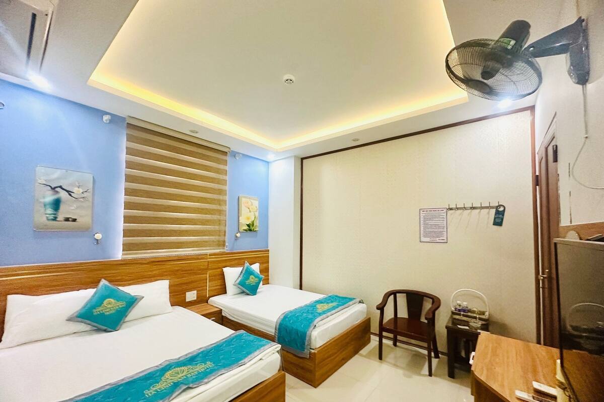 Ein Hotelzimmer mit zwei Betten, einem Schreibtisch, einem Stuhl, einem Ventilator und einer Schiebetür.
