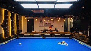 Ein Billardtisch mit blauer Spielvliesfläche, umgeben von Korbstühlen.