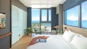 Ein modernes Hotelzimmer mit einem großen Bett, einem Balkon mit Meerblick und einem Essbereich mit Tisch und Stühlen.