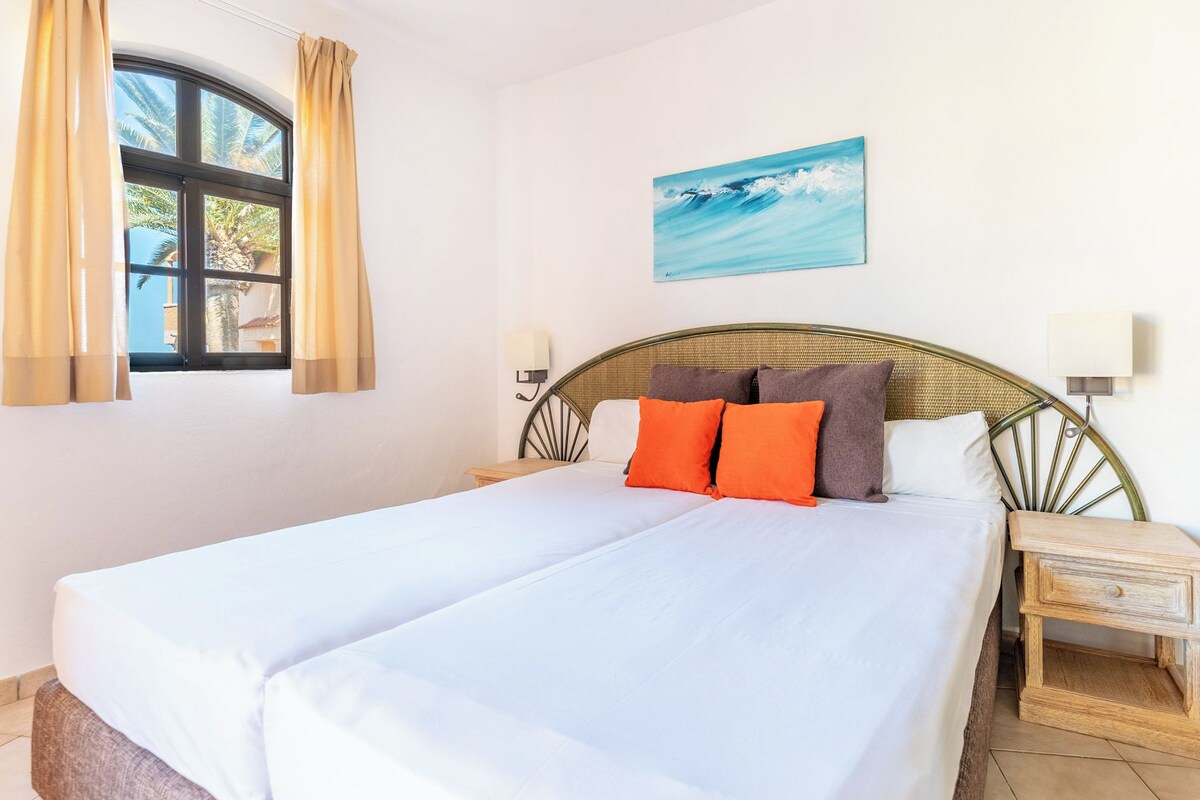 Una cama con ropa de cama blanca, un cabecero con diseño tejido, dos lámparas de noche y una mesita de noche de madera.