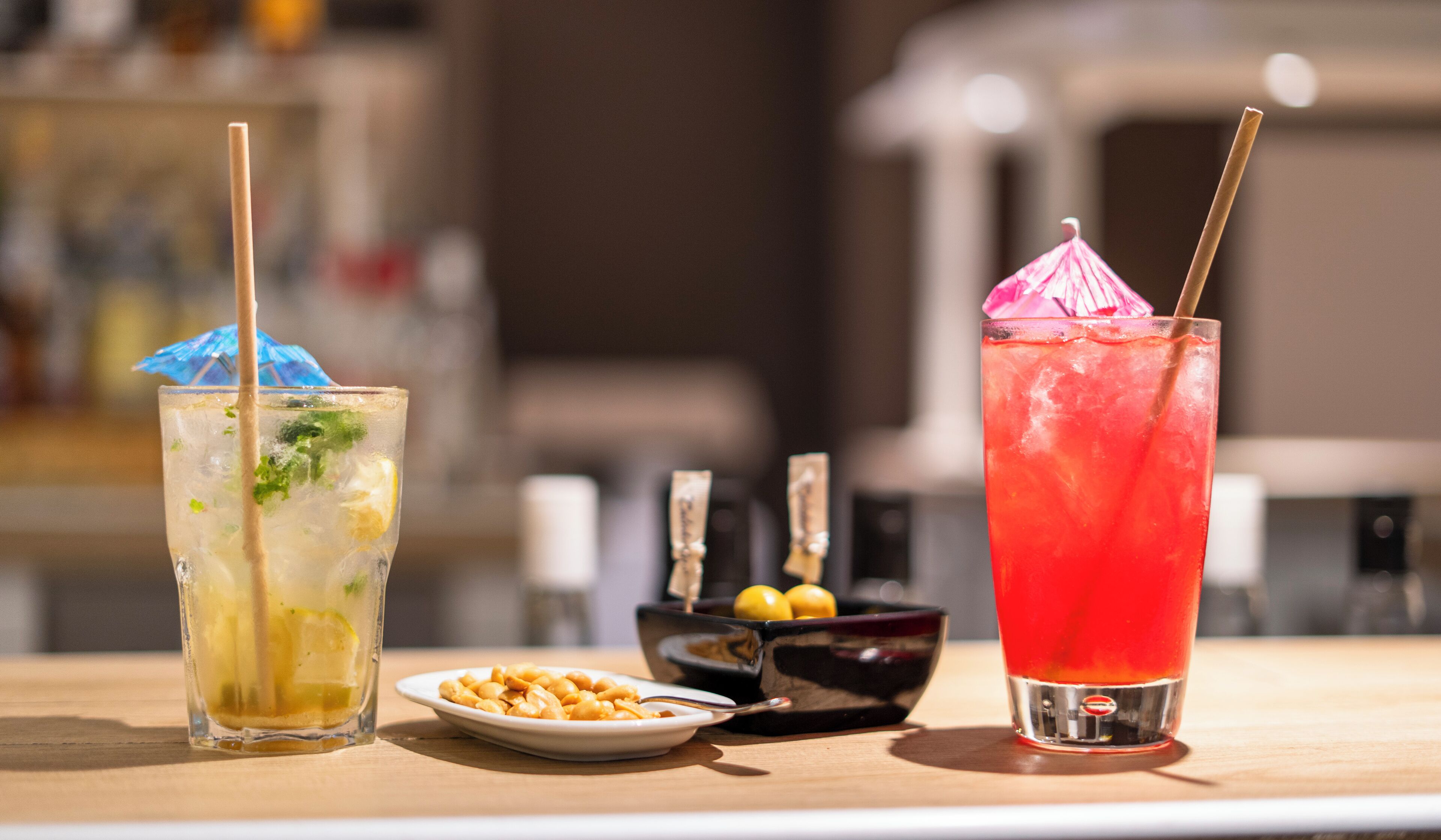 Dos bebidas sobre una barra, una con pajita y menta, la otra con un parasol rosa.