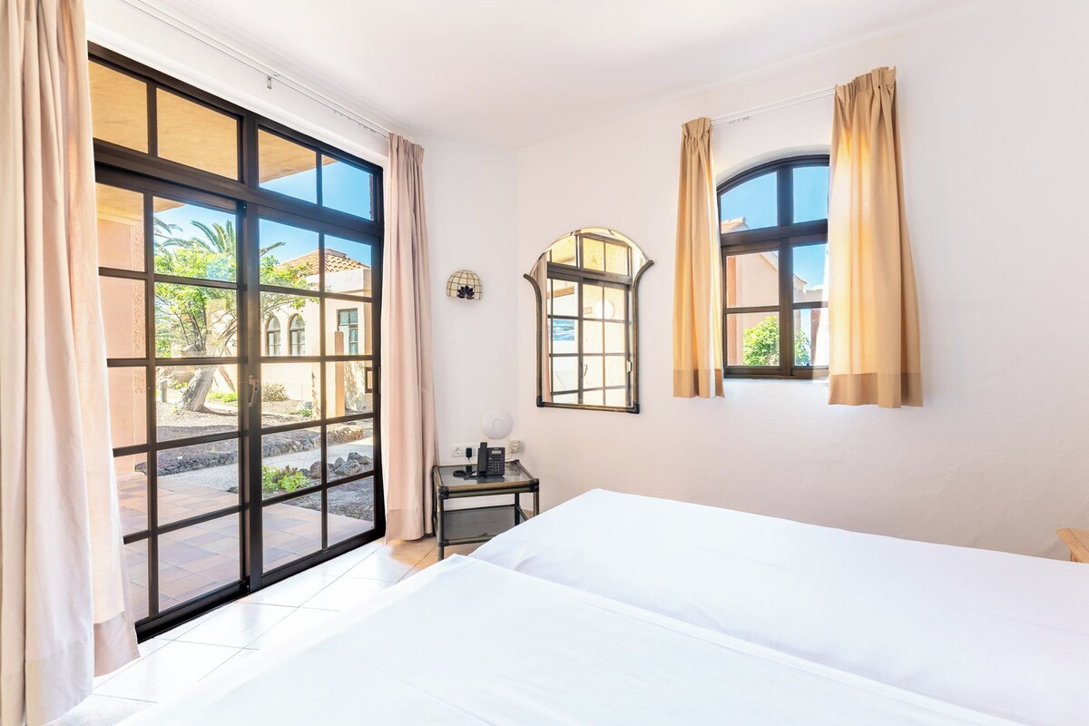 A hotel room with a large bed, two windows, and a small table with a telephone.