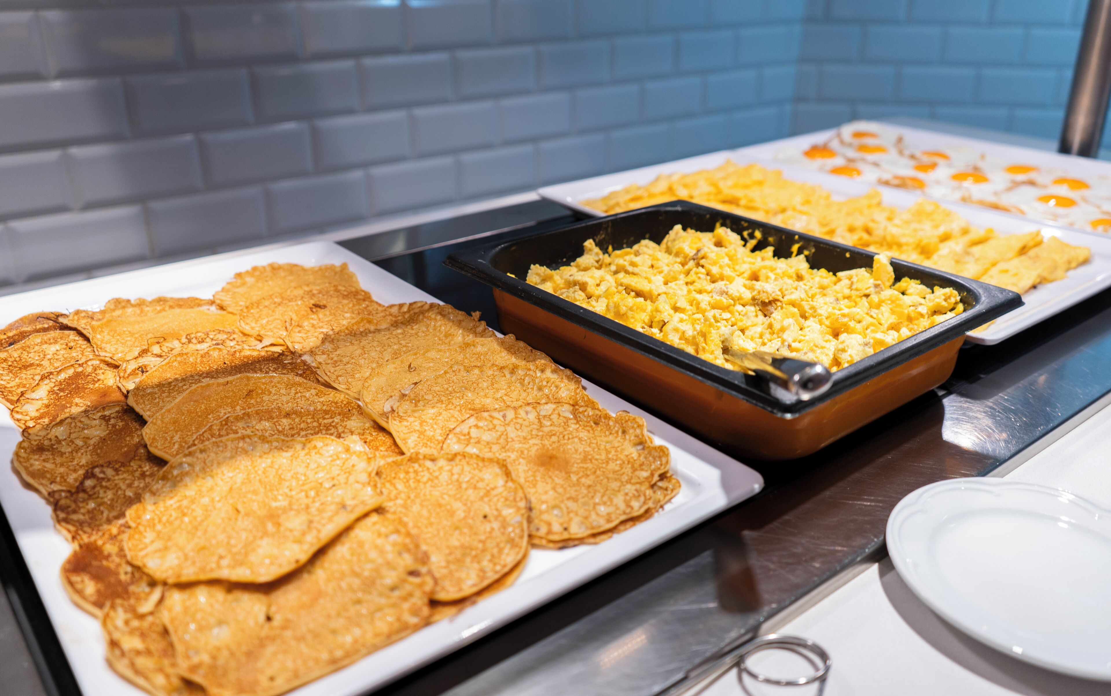 Un bufé con diversos alimentos, incluyendo panqueques, huevos revueltos y otras opciones para el desayuno.