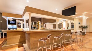 Un área de bar moderna con mostrador de madera, taburetes de metal y una pantalla de televisión.