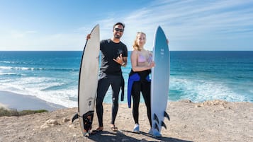 Two people holding surfboards on a rocky beach with the ocean in the background.
