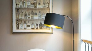 A framed liquor bottle collection on a wall, a black floor lamp, and a white chair with patterned cushions.