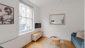 Un salon moderne avec une grande fenêtre, un téléviseur, une table ronde en bois et un canapé bleu.