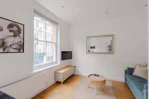 A modern living room with a large window, a television, a round wooden table, and a blue sofa.
