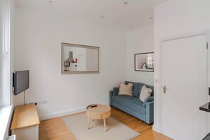 A living room with a sofa, a small wooden table, a round stool, a television, and a door.
