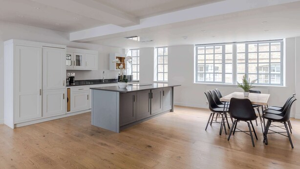 A modern kitchen with a large island, white cabinetry, and a dining area with black chairs. - Farringdon 3-Bed · 2 En-Suites · Lift · Sleeps 8 (London)