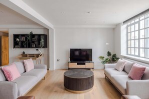 Un salon moderne avec un canapé, une table basse ronde, un téléviseur et une bibliothèque.