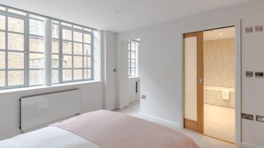 A bedroom with a large window, a radiator, a bed, and a sliding door leading to a bathroom. - Farringdon 3-Bed · 2 En-Suites · Lift · Sleeps 8 (London)