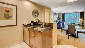 A modern hotel room with a kitchen area, a dining table with chairs, a sofa, and a large window offering a city view. - SVS: Designer Remodeled 1BD | Strip View Balcony | Signature at MGM (Las Vegas)