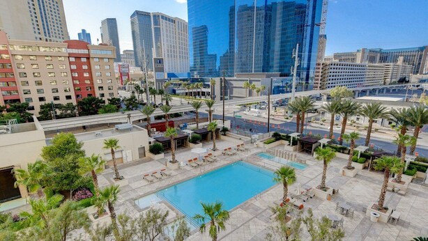 A rooftop pool area with palm trees and lounge chairs, surrounded by high-rise buildings. - SVS: Designer Remodeled 1BD | Strip View Balcony | Signature at MGM (Las Vegas)
