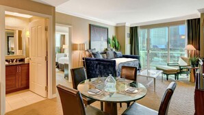 A hotel room with a balcony, a dining area with a glass table, a sofa, and a large window with a city view. - SVS: Designer Remodeled 1BD | Strip View Balcony | Signature at MGM (Las Vegas)