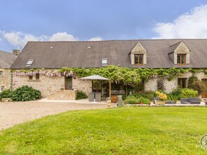 Un bâtiment en pierre doté d’un toit en pente, d’un patio couvert et d’une pelouse bien entretenue.