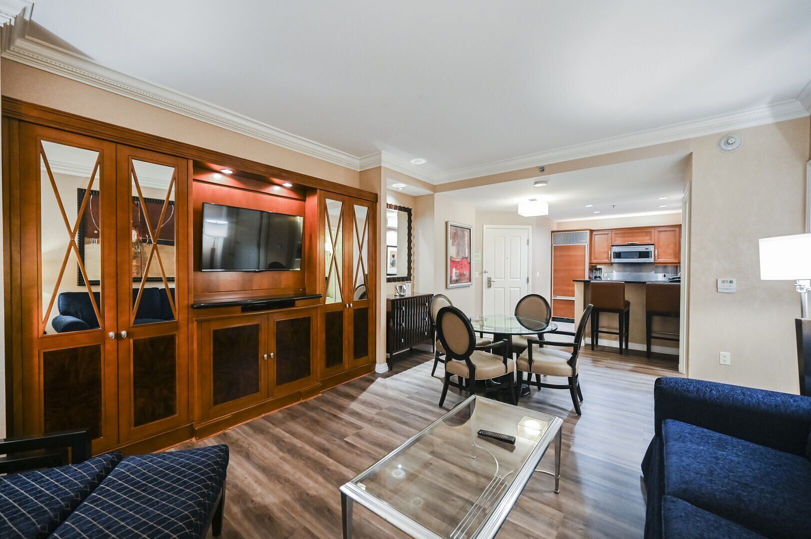A modern living room with a glass coffee table, a TV, and a dining area with chairs.