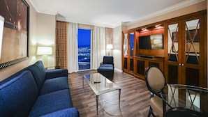 A hotel room with a large sofa, a glass coffee table, a TV, and a view of the city at night. - 1BD/2BA • Balcony • No Resort Fee • Free Parking E24I2 (Las Vegas)