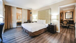 A hotel room with a large bed, a desk with a chair, a vanity with a mirror, and a bathroom visible through a glass door. - 1BD/2BA • Balcony • No Resort Fee • Free Parking E24I2 (Las Vegas)