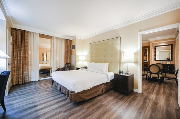 A hotel room with a large bed, a desk with a chair, a vanity with a mirror, and a bathroom visible through a glass door. - 1BD/2BA • Balcony • No Resort Fee • Free Parking E24I2 (Las Vegas)