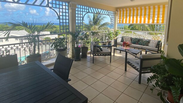 Een balkon met uitzicht op de oceaan, een plafondventilator en een zithoek met een bank en stoelen.
