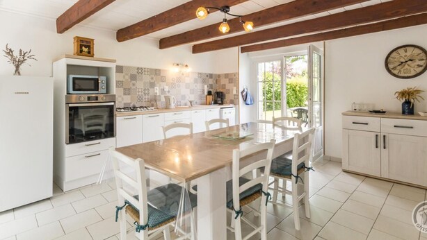 A kitchen with white cabinets, a wooden table, and a clock on the wall. - Peaceful country house with enclosed garden (Muneville-sur-Mer)