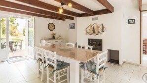 A dining area with a wooden table and chairs, a fireplace, and a view through a glass door to an outdoor patio. - Peaceful country house with enclosed garden (Muneville-sur-Mer)