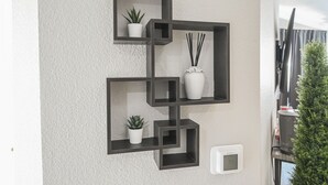 A wall-mounted black shelving unit with potted plants and a thermostat. - SVS: Bright 1BD Condo | Gated Community | Pool | Near the Strip (Las Vegas)