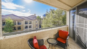 A balcony with two wicker chairs and a small table, overlooking a residential area with buildings and trees. - SVS: Bright 1BD Condo | Gated Community | Pool | Near the Strip (Las Vegas)