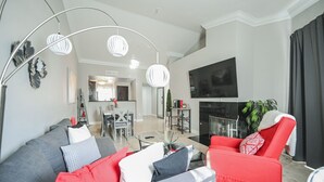 A modern living room with a grey sofa, red armchair, and a flat-screen TV mounted on the wall. - SVS: Bright 1BD Condo | Gated Community | Pool | Near the Strip (Las Vegas)