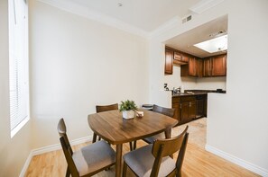 Un coin repas avec une table et des chaises en bois, une plante en pot et une cuisine en arrière-plan.