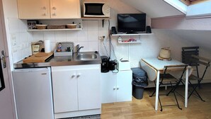 Una cucina compatta con mobili bianchi, un forno a microonde, una televisione, un lavandino e un piccolo frigorifero.