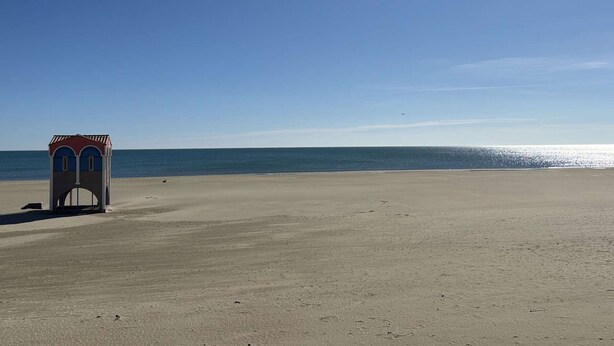 A beach with a small building, clear sky, and calm sea.