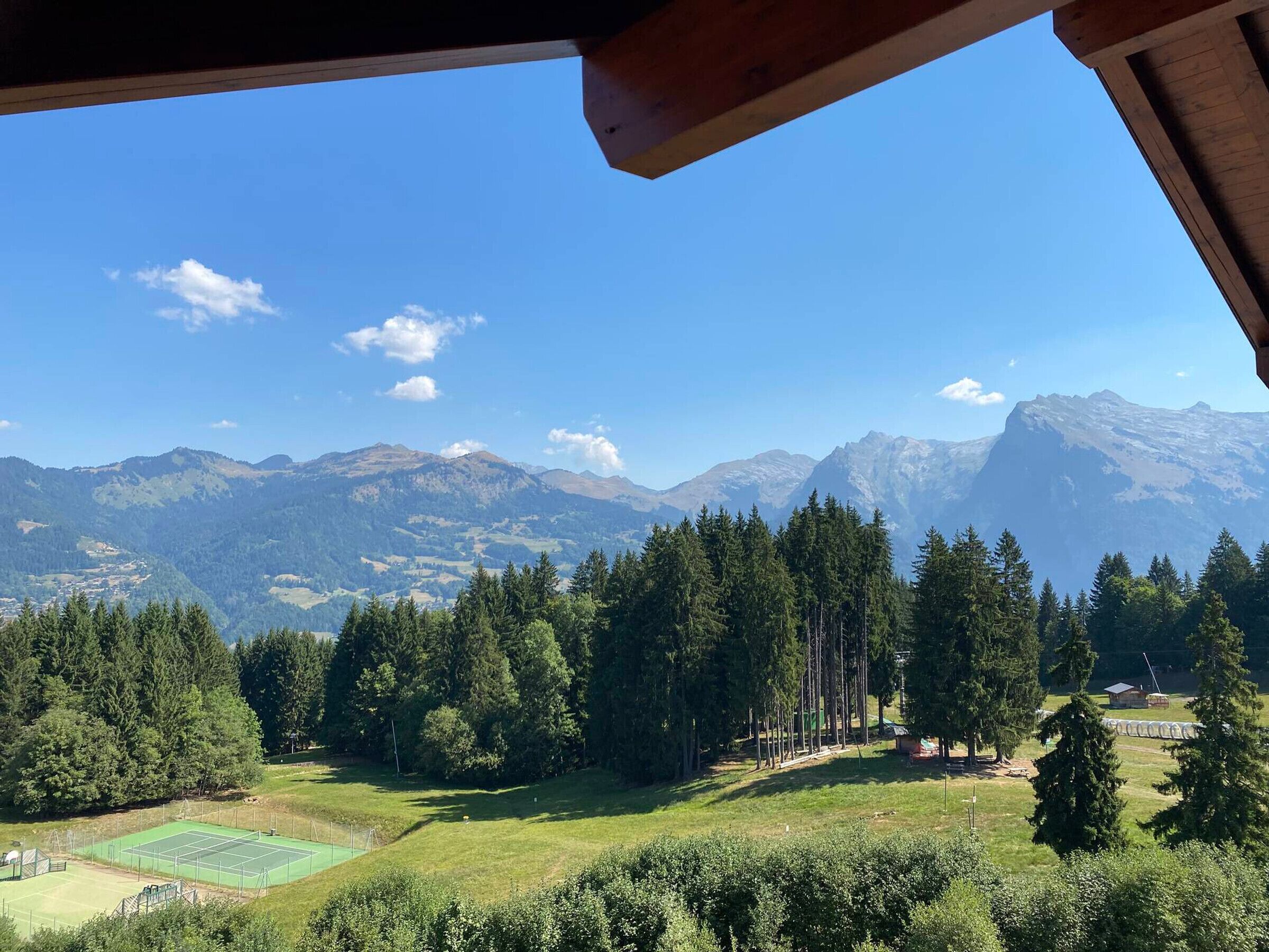 A view of a tennis court surrounded by dense forest and mountains.