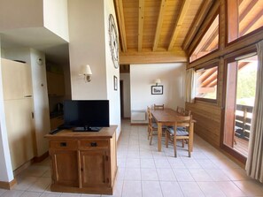 A cozy room with a wooden dining table, chairs, a television on a wooden cabinet, and a window with curtains.