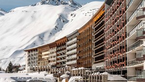 A hotel with multiple balconies, a ski slope in the background, and snow-covered surroundings.