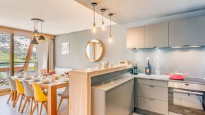 A modern kitchen with a dining area, featuring a large island, stainless steel appliances, and a view of the outdoors.