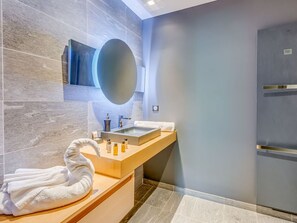 Un baño moderno con pared de mármol, un espejo grande, un lavabo con una toalla y una zona de ducha.
