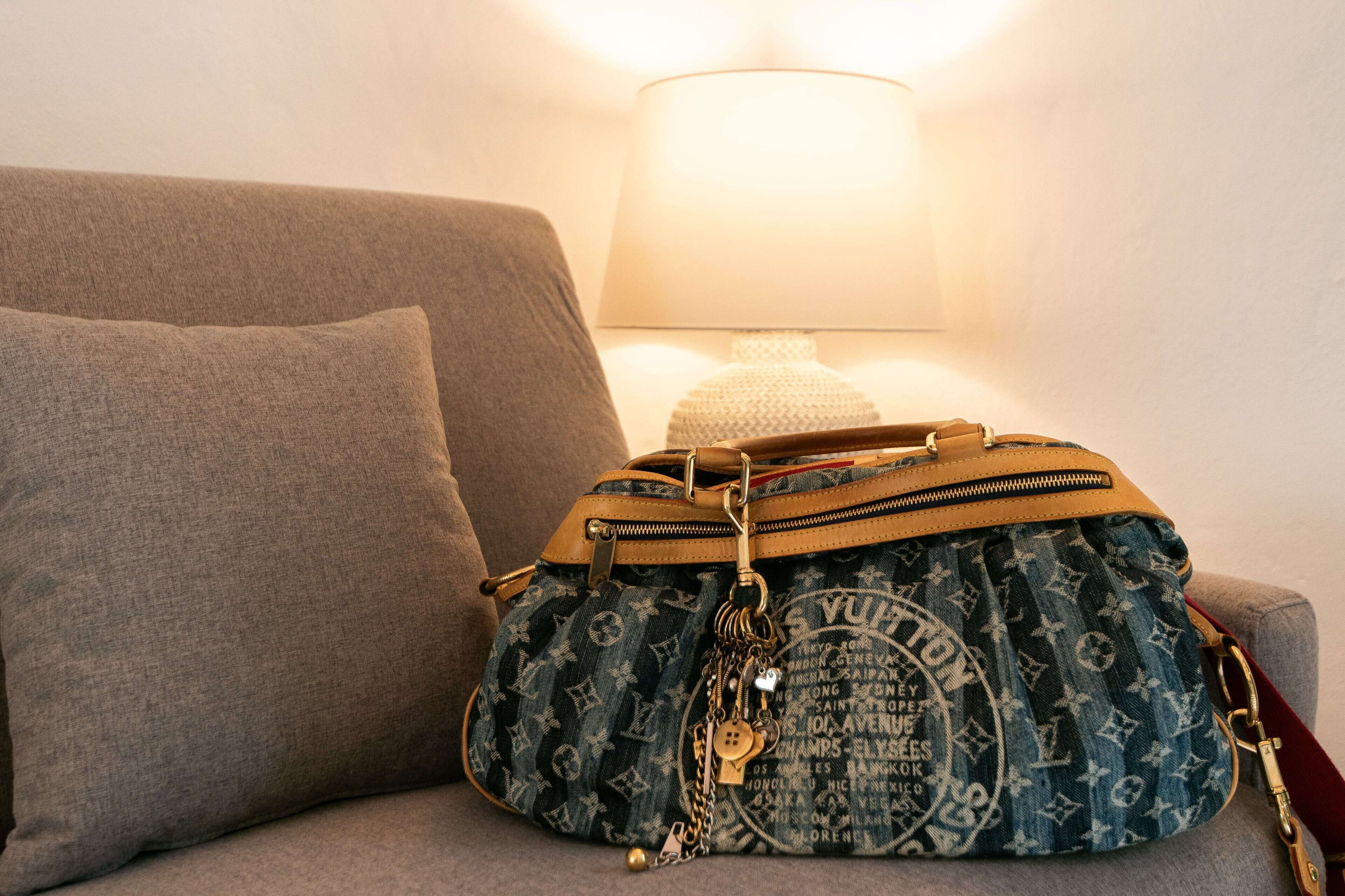 En grå soffa med en enda kudde och en Louis Vuitton-handväska placerad på den.