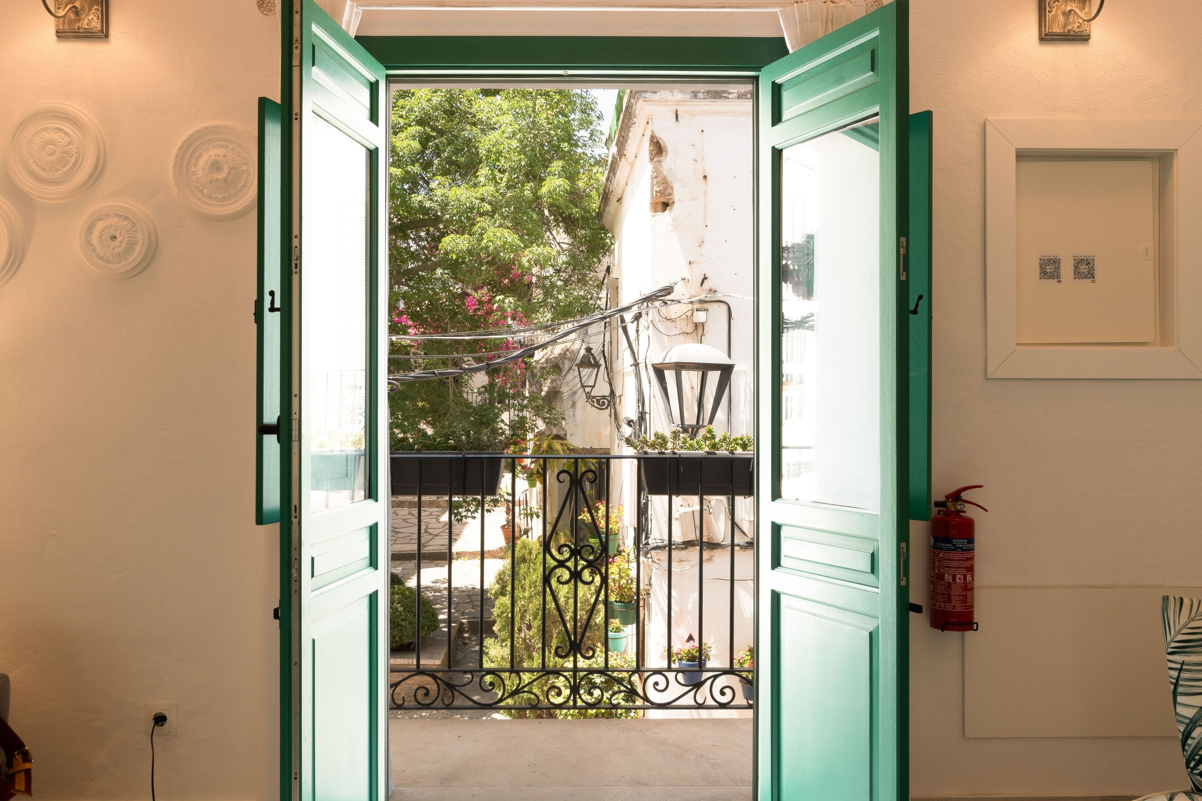 An open door leading to a balcony with a view of a street and buildings.
